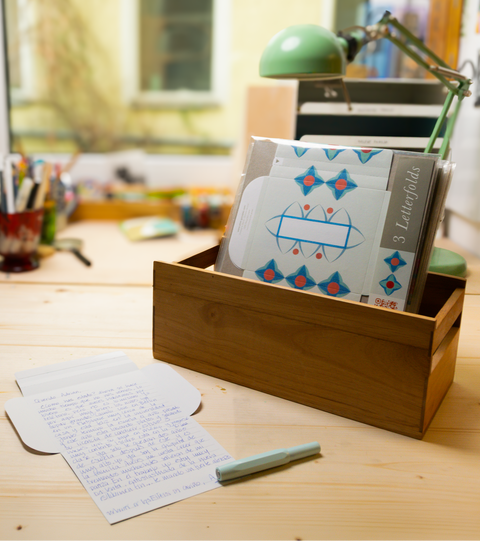 Three turquoise floral letterfolds and an open letterfold arranged in a stylish stationery desk setting.