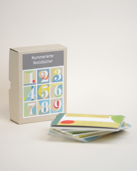 Bundle box of 9 numbered DIN A6 notebooks made from 100% recycled paper, eco-friendly and hand-bound, front view.