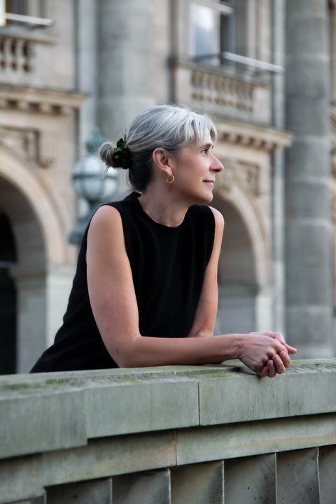 Portrait of the stationery artist Ame González, leaning on a bridge in Berlin with a historic building in the background – sustainable design inspiration.